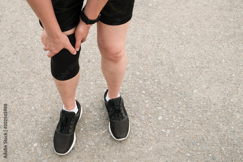 Closeup of runner woman wearing knee support to prevent and reduce knee pain from running. Conceptual of injury from running workout. Closeup of runner woman wearing knee support to prevent and reduce knee pain from running. Conceptual of injury from running workout.