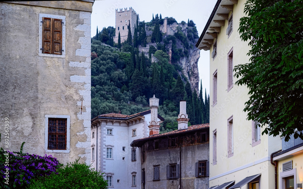 Street with Castello di Arco on rock at Garda lake of Trentino in Italy. Cityscape with ruins of castle on hill in Trento near Riva del Garda. Remains of tower and Italian landmark in mountains.