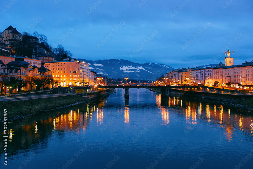 Panorama of Salzburg Old city and bridge over Salzach River in Austria in evening. Landscape and cityscape of Mozart city in Europe at winter at night. Panoramic view of old Austrian town street.