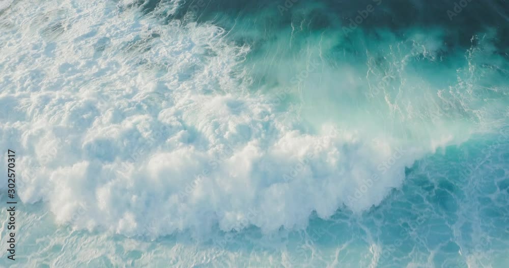 Aerial view of a blue ocean wave breaking with spray at sunset, white water tsunami wave rushing towards the camera, ocean white water textures