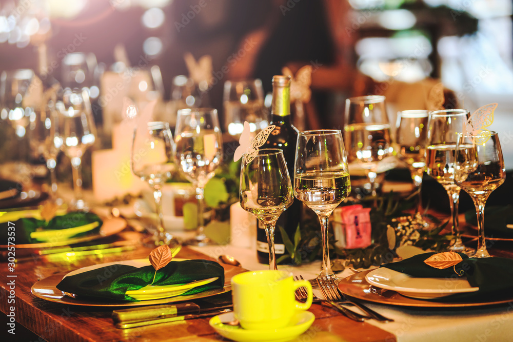 Some wine glasses, plates, forks and green briefcases for event celebration. Beautiful dinner table setting. Vintage decoration of reception table. Elegant arrangement of the holiday tableware. Some wine glasses, plates, forks and green briefcases for event celebration. Beautiful dinner table setting. Vintage decoration of reception table. Elegant arrangement of the holiday tableware.
