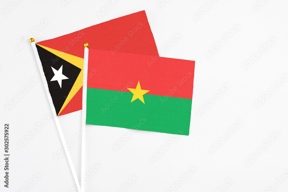 Burkina Faso and East Timor stick flags on white background. High quality fabric, miniature national flag. Peaceful global concept.White floor for copy space.