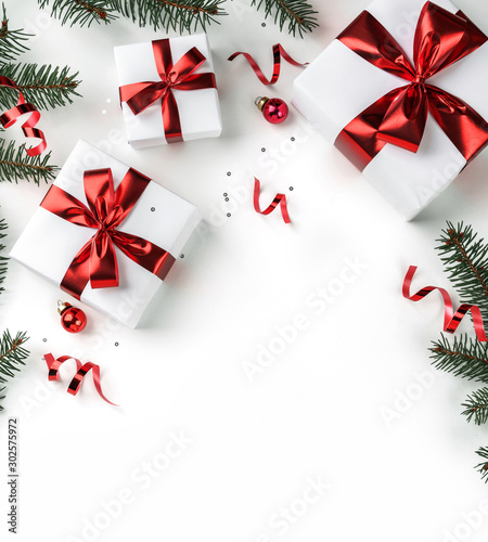 Christmas fir branches, gift boxes with red ribbon, red decoration, sparkles and confetti on white background. Xmas and New Year greeting card, winter holiday. Flat lay, top view