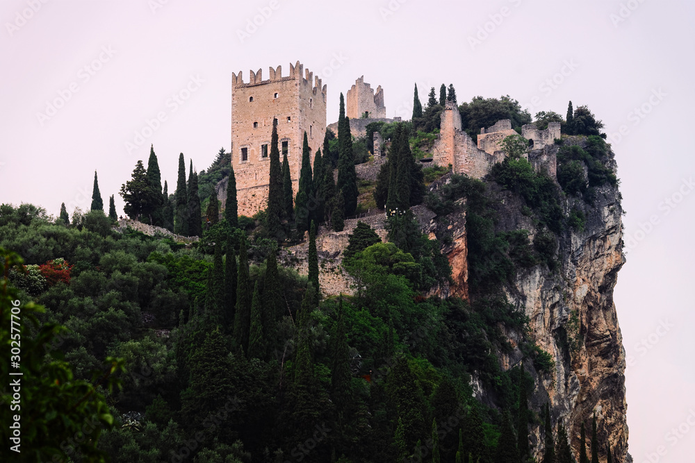 Landscape with Castello di Arco in rock at Garda lake of Trentino, Italy in evening. Scenery with ruins of castle on hill in Trento near Riva del Garda. Remains of tower in mountains at dawn.