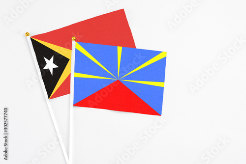 Reunion and East Timor stick flags on white background. High quality fabric, miniature national flag. Peaceful global concept.White floor for copy space.