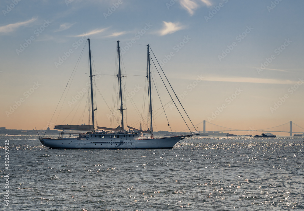 Sail boat traveling in New York's Hudson Bay in front of a bridge during the golden hour of sunet.
