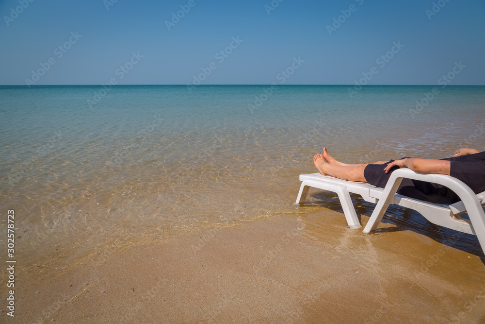 Vacation on tropical beach Woman's legs on the beach bed with clear ocean water Vacation on tropical beach Woman's legs on the beach bed with clear ocean water