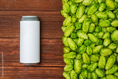 A beer can, green cones of hops on wooden background. Craft canned beer with fresh hops. Top view