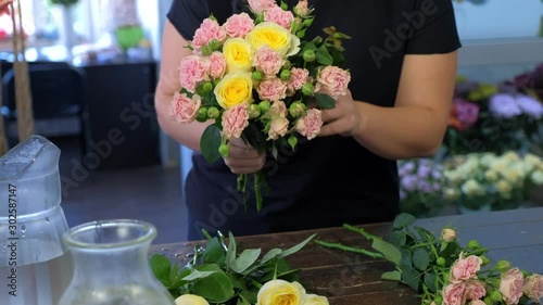 Floral business concept. Professional woman florist making flowers bunch bouquet from different sorts of roses over table in flower shop, hands closeup. Working day in floristic studo store salon.