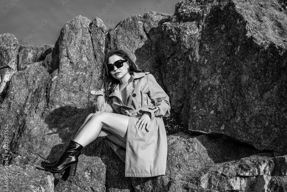 young beautiful brunette girl in spring coat and sunglasses outdoors in autumn sun. attractive young woman in autumn image. monochrome, black and white photography young beautiful brunette girl in spring coat and sunglasses outdoors in autumn sun. attractive young woman in autumn image. monochrome, black and white photography
