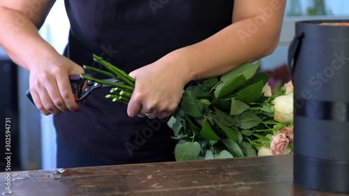 Working day in floristic studo store salon. Professional florist woman prepares flowers to bunch cuts rose stems with cutters in shop, closeup hands. Floral business concept.