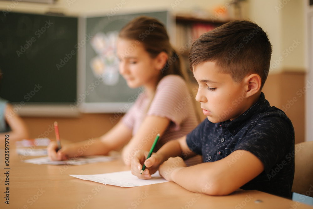 Group of school kids with pens and notebooks writing test in classroom. education, elementary school, learning and people concept Group of school kids with pens and notebooks writing test in classroom. education, elementary school, learning and people concept