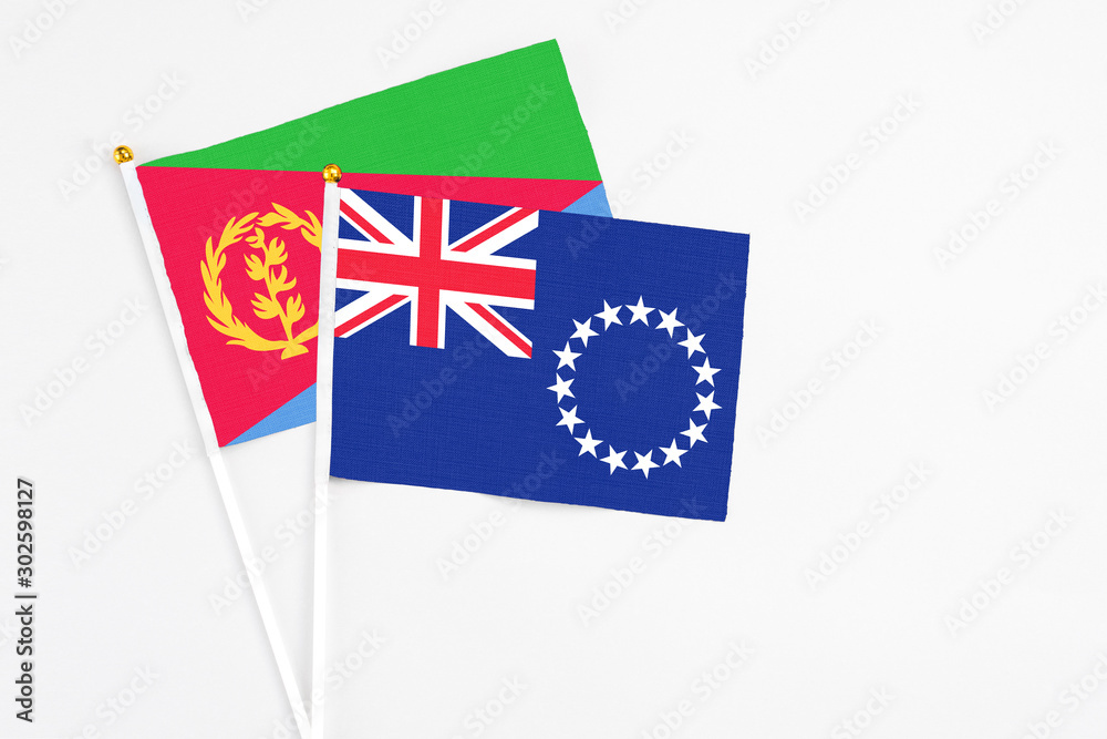 Fototapeta premium Cook Islands and Eritrea stick flags on white background. High quality fabric, miniature national flag. Peaceful global concept.White floor for copy space.