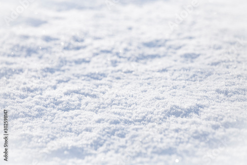 Background of sparkling fresh white snow texture with light blue sky reflection tone.