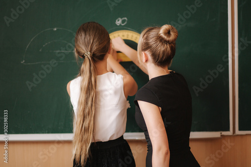 Teacher help girl by the blackboard. Young female teacher study