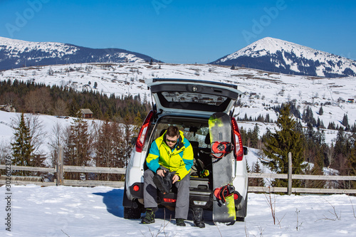 man sitting in car trunk changing for snowboard