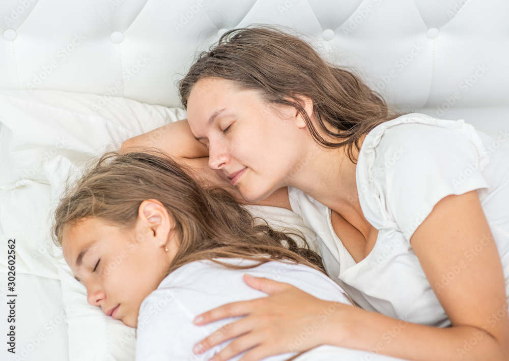 Mother and daughter sleep together on the bed at home. Top down view Mother and daughter sleep together on the bed at home. Top down view