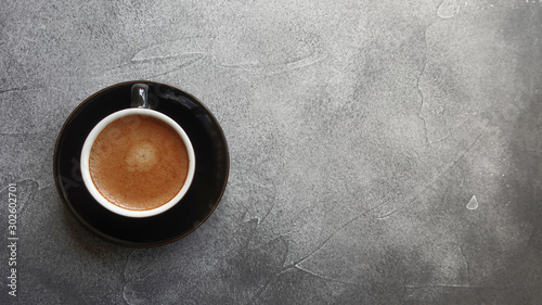 Cup of freshly brewed espresso on a saucer on a gray textured background