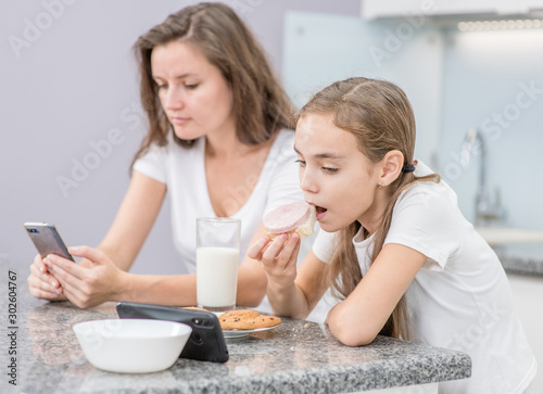 Tableau sur toile Mom and her daughter use smartphone while having breakfast at home