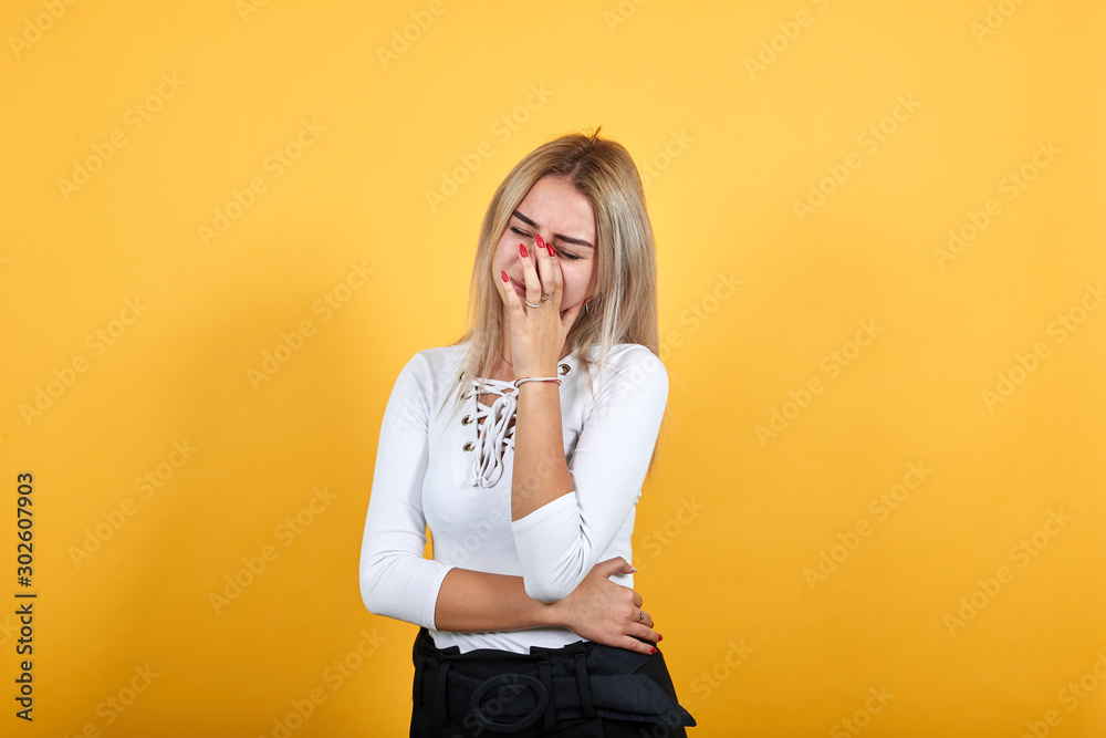Pretty young caucasian blonde woman wearing nice white shirt over orange background, looking bored, tired, thinking about issue, keeping hands on mouth, eyes closed Pretty young caucasian blonde woman wearing nice white shirt over orange background, looking bored, tired, thinking about issue, keeping hands on mouth, eyes closed