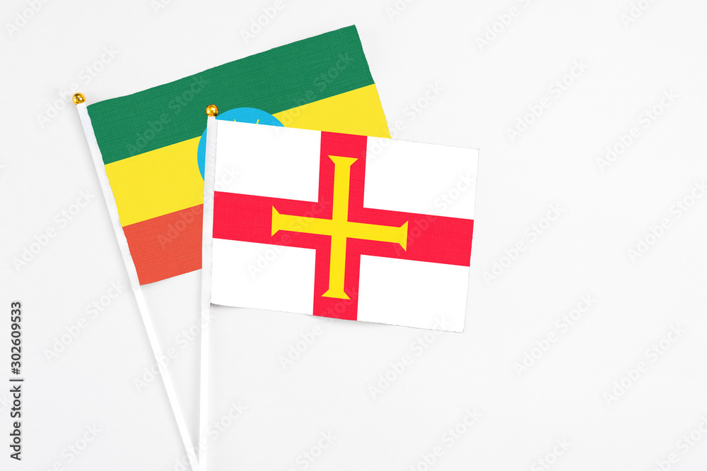 Guernsey and Ethiopia stick flags on white background. High quality fabric, miniature national flag. Peaceful global concept.White floor for copy space.