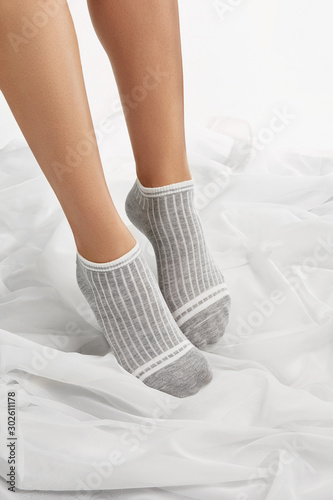 Cropped shot of a girl's feet, staying on a floor. There are short grey socks with white stripes on her feet. The photo was taken on a white background. 