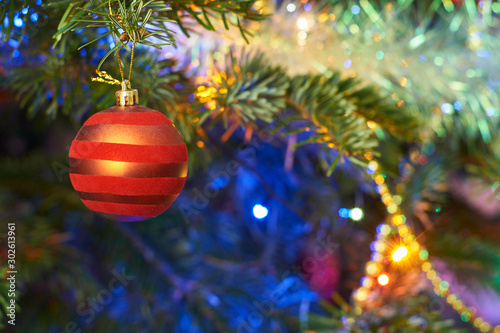 New Year's composition, Christmas decorations. Red christmas ball hanging on a fir-tree against the background of a luminous Christmas garland and silvery tinsel