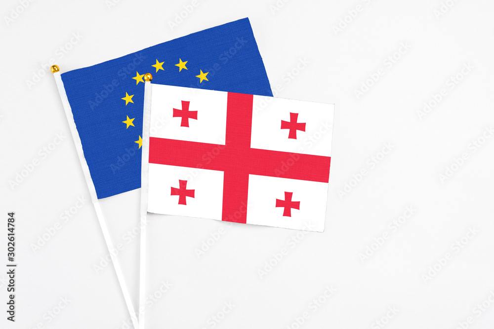 Georgia and European Union stick flags on white background. High quality fabric, miniature national flag. Peaceful global concept.White floor for copy space.