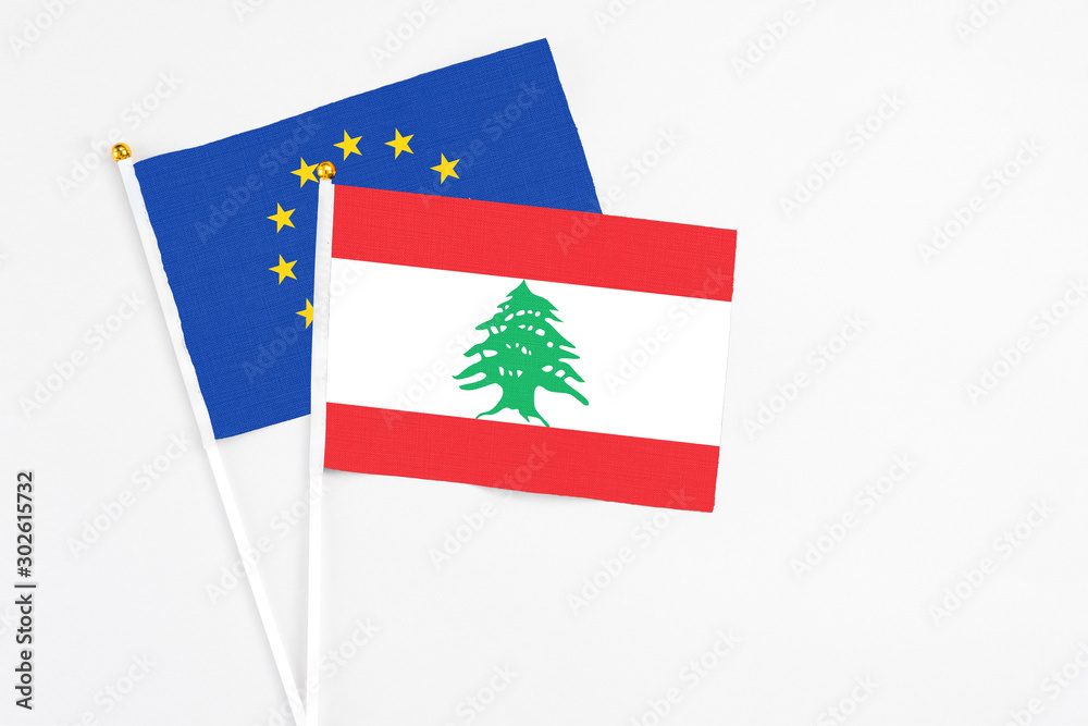 Naklejka premium Lebanon and European Union stick flags on white background. High quality fabric, miniature national flag. Peaceful global concept.White floor for copy space.
