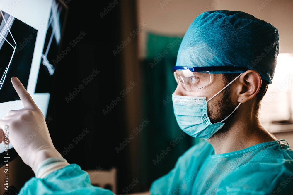 surgeon in uniform and glasses examines an X-ray image of a bone fracture in the operating room. surgeon in uniform and glasses examines an X-ray image of a bone fracture in the operating room.