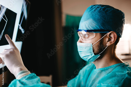 surgeon in uniform and glasses examines an X-ray image of a bone fracture in the operating room.