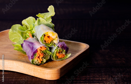Fresh asian vegetable spring roll wrap with  rice paper with green lettuce, carrot, corn, purple cabbage on wooden plate and table. Clean food, healthy, light appitizer concept. Free copy space on rig