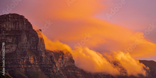 Golden cloudy sunset or sunrise over a mountain range in Camps Bay, Cape Town.
