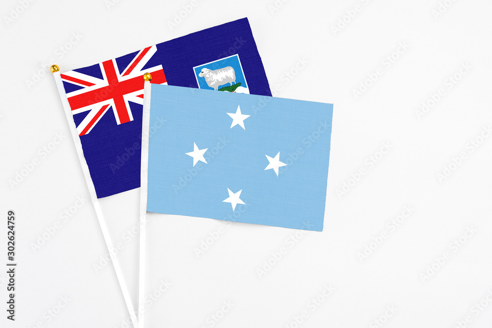 Fototapeta premium Micronesia and Falkland Islands stick flags on white background. High quality fabric, miniature national flag. Peaceful global concept.White floor for copy space.