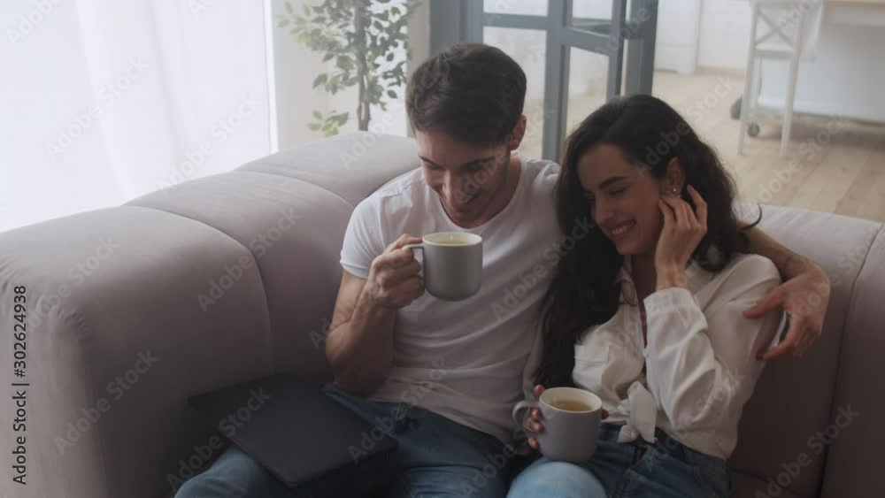 Smiling couple drinking tea at home together. Sexy man and woman smiling at sofa Smiling couple drinking tea at home together. Sexy man and woman smiling at sofa