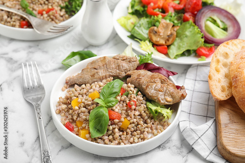 Tasty buckwheat porridge with meat on white marble table