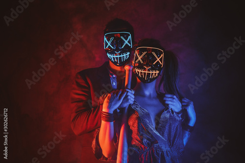 Portrait of elegant couple in scary masks with baseball bat in hands.