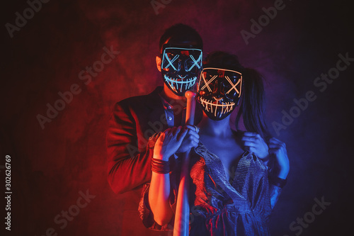 Portrait of elegant couple in scary masks with baseball bat in hands.