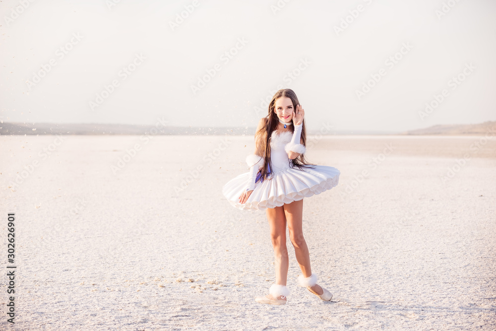 Tender young ballerina dancer in a snow-white tutu dress and white pointe shoes on a salty dried lake. Fantastic landscape and a girl ballerina Tender young ballerina dancer in a snow-white tutu dress and white pointe shoes on a salty dried lake. Fantastic landscape and a girl ballerina