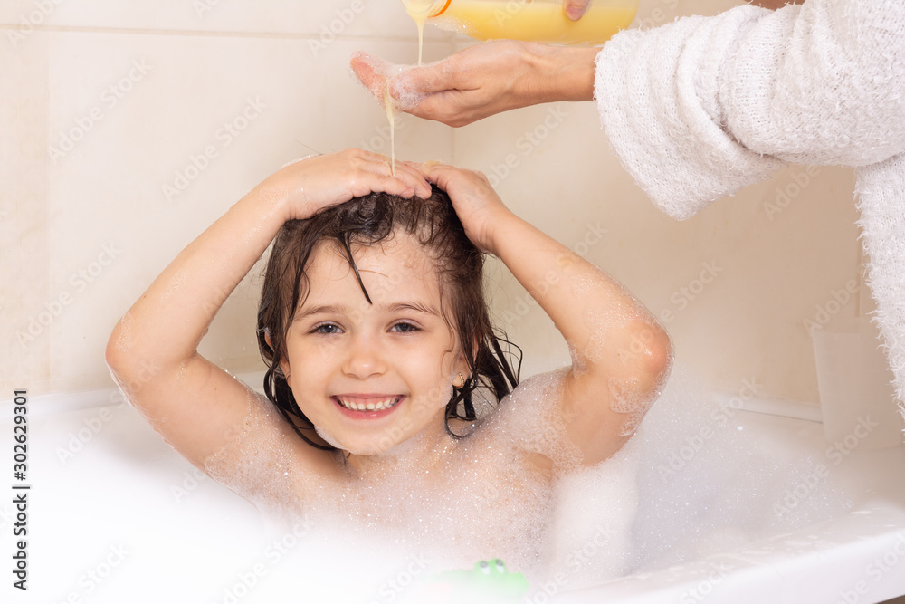 Foto de Shampoo hair and soap for children. Kid bathing in large tub. Baby  girl with foam in hair. Mother washing child hair with shampoo in the  shower. do Stock | Adobe