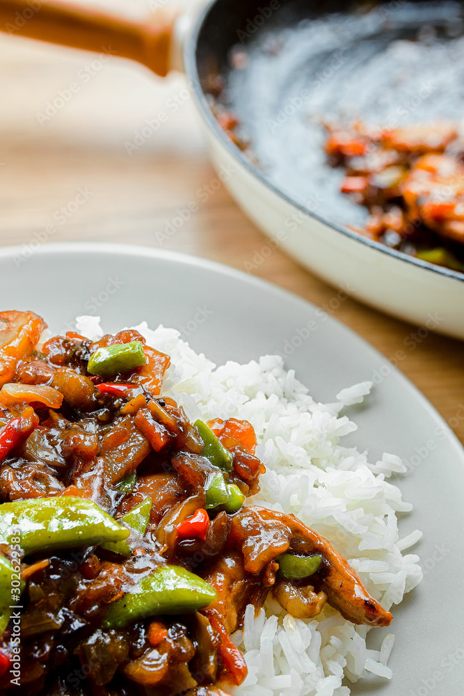 Portion of stir fry vegetables and rice on a white plate with frying pan in background Portion of stir fry vegetables and rice on a white plate with frying pan in background