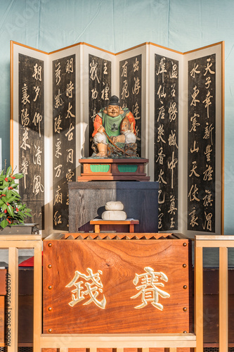 Wooden statue of the Shinto deity Ebisu with a screen, a kagami mochi rice cake and a donation box where is inscribed saisen which means money in the seiunji zen temple of tokyo photo