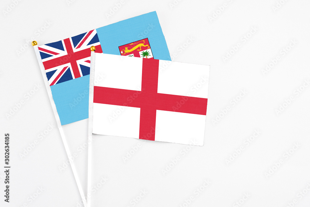 England and Fiji stick flags on white background. High quality fabric, miniature national flag. Peaceful global concept.White floor for copy space.