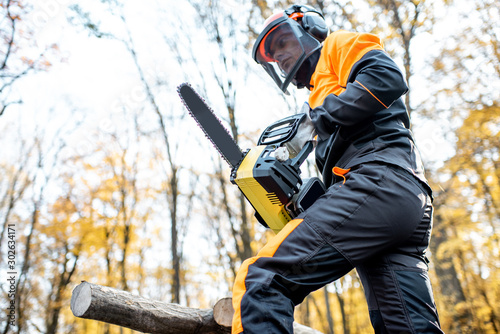 Professional lumberjack in protective workwear working with a chainsaw in the forest. Woodcutter makes a logging outdoors photo