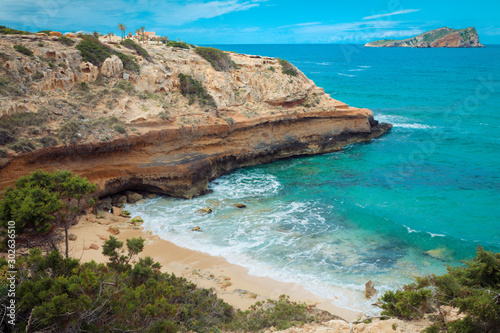 View of high cliffs above the turquoise sea line in Cala Escondida in Ibiza, Spain