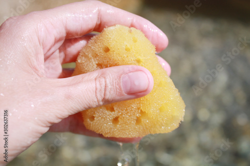 Obraz na płótnie Sea sponge in the hand in sea water on the beach background. w salonie