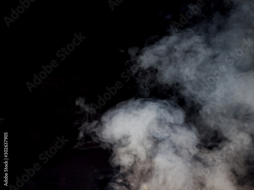 Light smoke pours and flows on a dark background. Studio photography