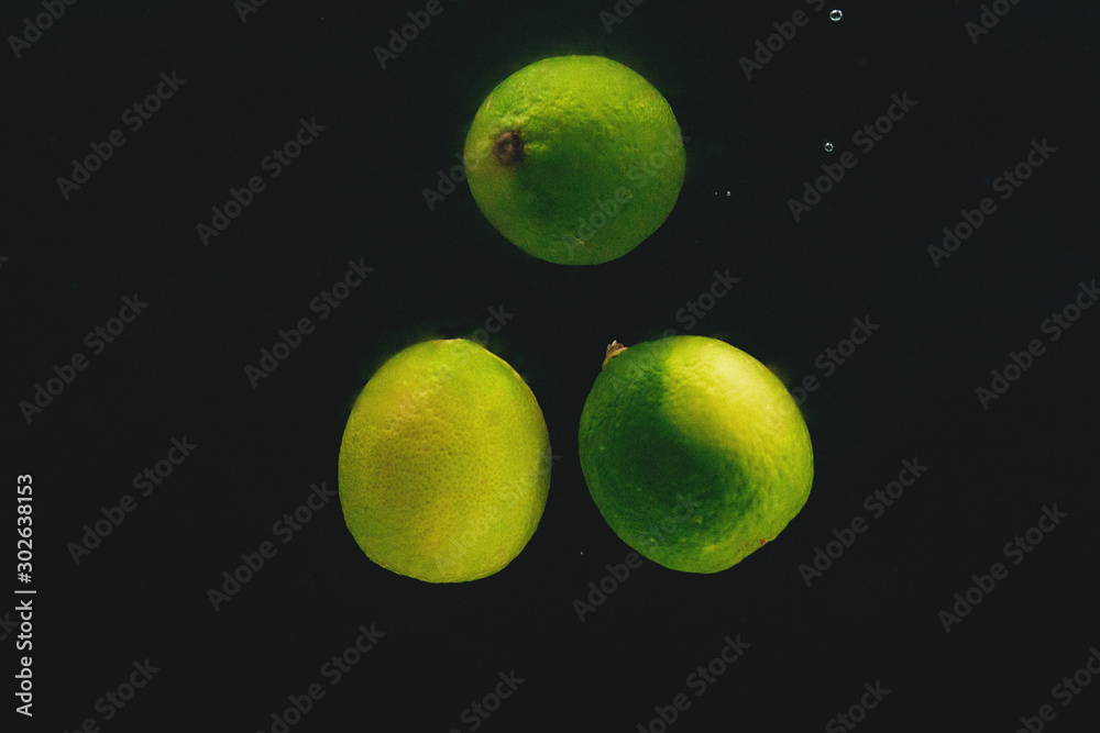 Green limes in water on a black background.