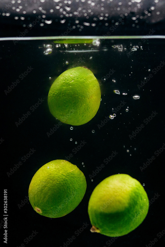 Green limes in water on a black background.