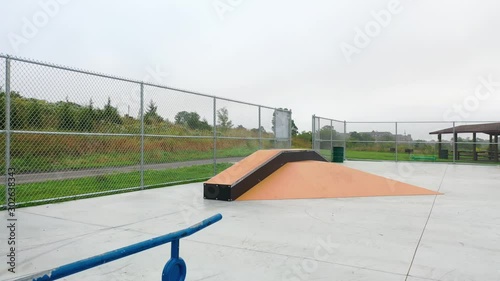 Slowly skating towards a skateboard shaped rail and a ramp in a skatepark photo